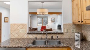 A kitchen with granite countertops, a double sink, wooden cabinets, a pendant light, and a view into a living room with a fireplace. - Corazon Condo Unit 2, 2 Bed / 2 Bath, Luxury Style Condo (Santa Fe)