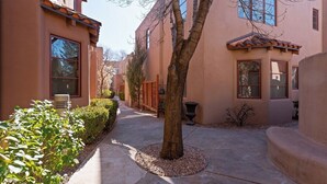 A narrow pathway flanked by buildings with stucco walls and tiled roofs, leading to a tree-lined area. - Corazon Condo Unit 2, 2 Bed / 2 Bath, Luxury Style Condo (Santa Fe)