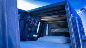 Een kleine, afgesloten ruimte met een stapelbed, een tafeltje en een wandlamp.