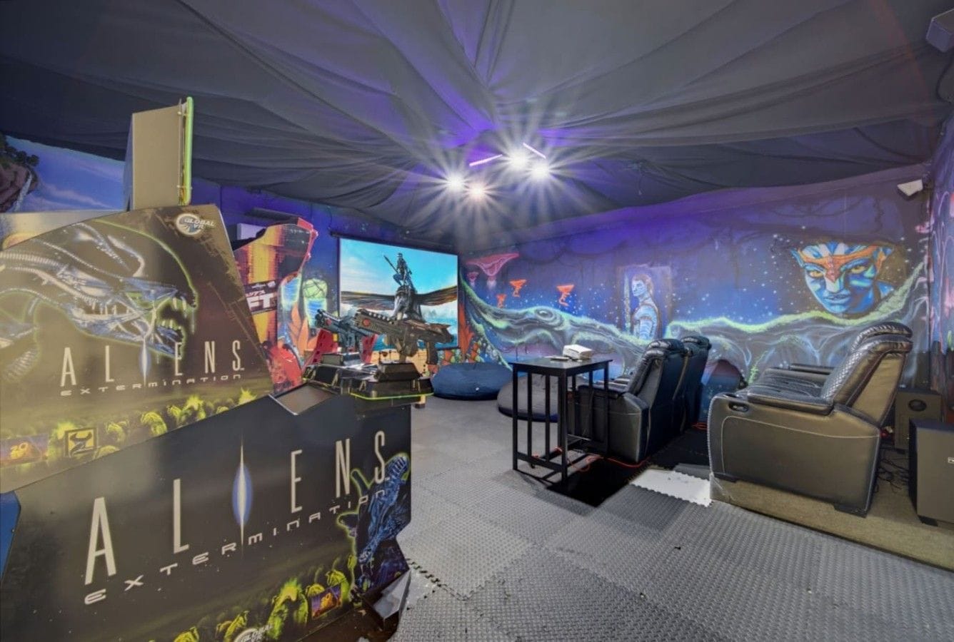 Une salle de jeux équipée d’un grand écran, de fauteuils de jeu et d’un mur décoré d’œuvres d’art sur le thème de l’espace.
