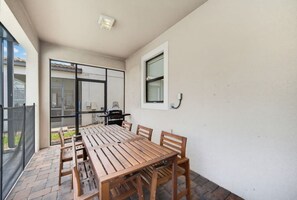 Een terras met een houten tafel en stoelen, een barbecue en een schuifdeur naar een achtertuin.