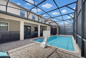 An indoor swimming pool with a slide, surrounded by a covered patio area with a brick floor. - 6BR Magic Mansion – Ultimate Disney Escape (Four Corners)