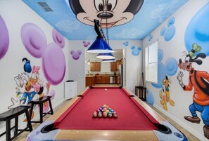 A pool table with a red felt surface, surrounded by cartoon character murals on the walls.