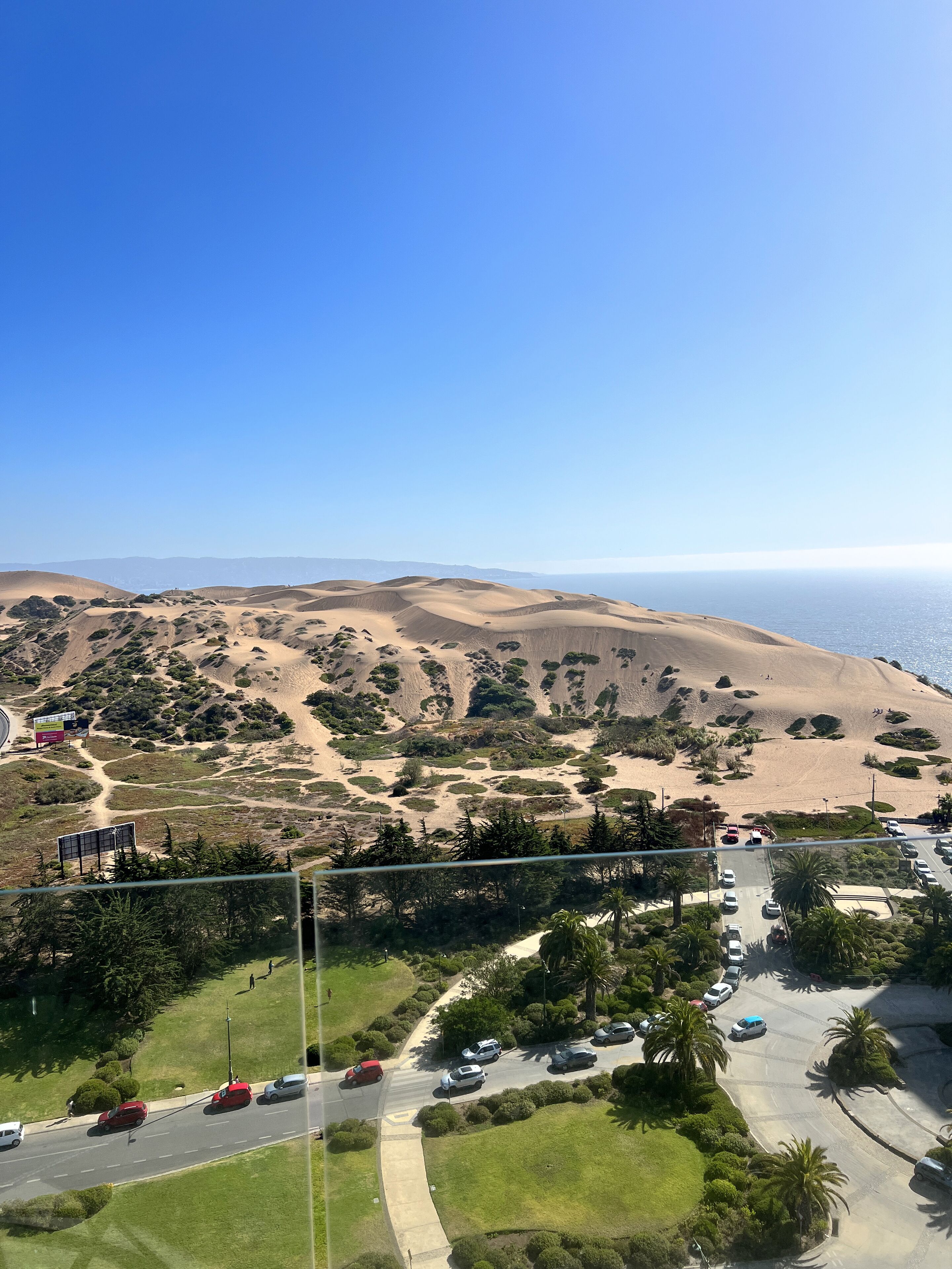 A coastal landscape with rolling sand dunes, a parking area, and a road leading to a beach.