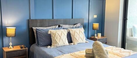 A bedroom with a large bed, two bedside tables, a nightstand, a window with a view, and a ceiling light fixture.