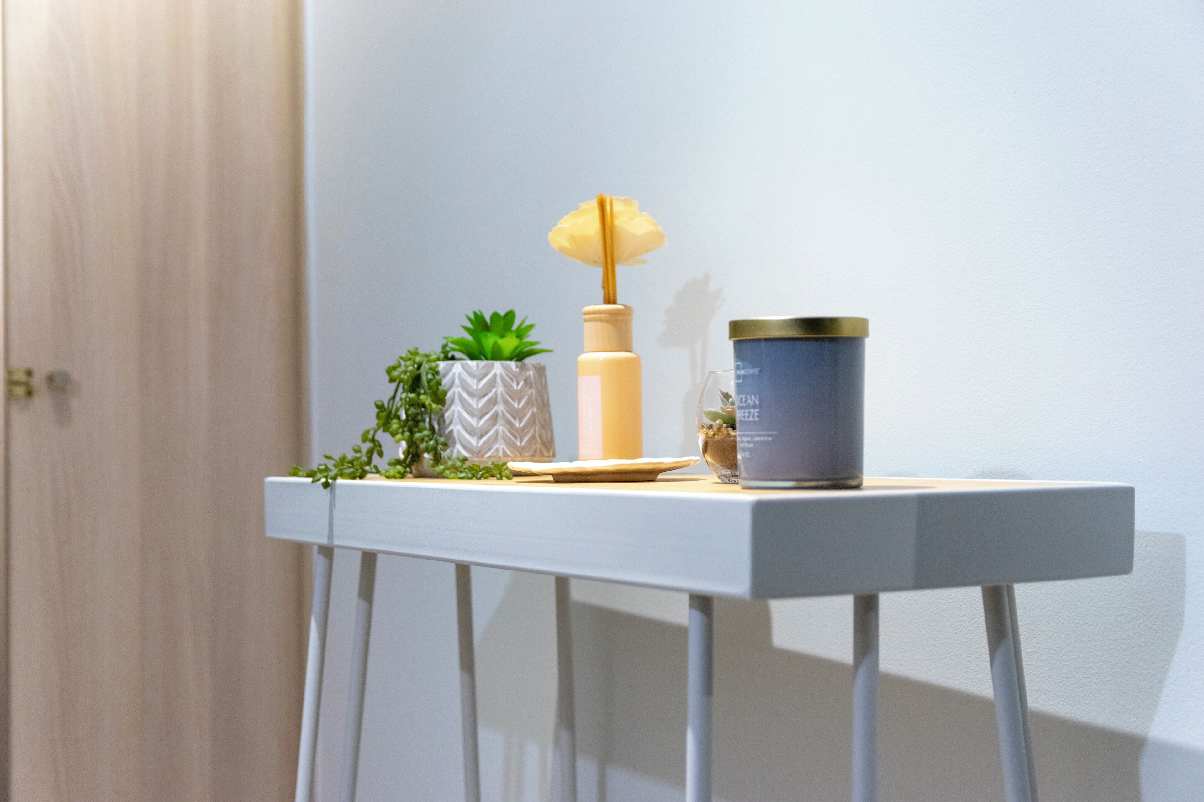 A white table with a potted plant, a candle, and a container.