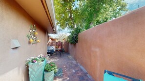 Un petit patio extérieur, avec un sol en briques, une table entourée de chaises et un jardinier mural orné de fleurs.
