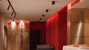 A hotel corridor with a red accent wall, a reception desk, and a seating area. - Hotel Chicago (Shkodër)