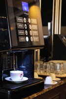 A coffee machine with a digital interface, a cup of coffee on a saucer, and a glass container on the counter.