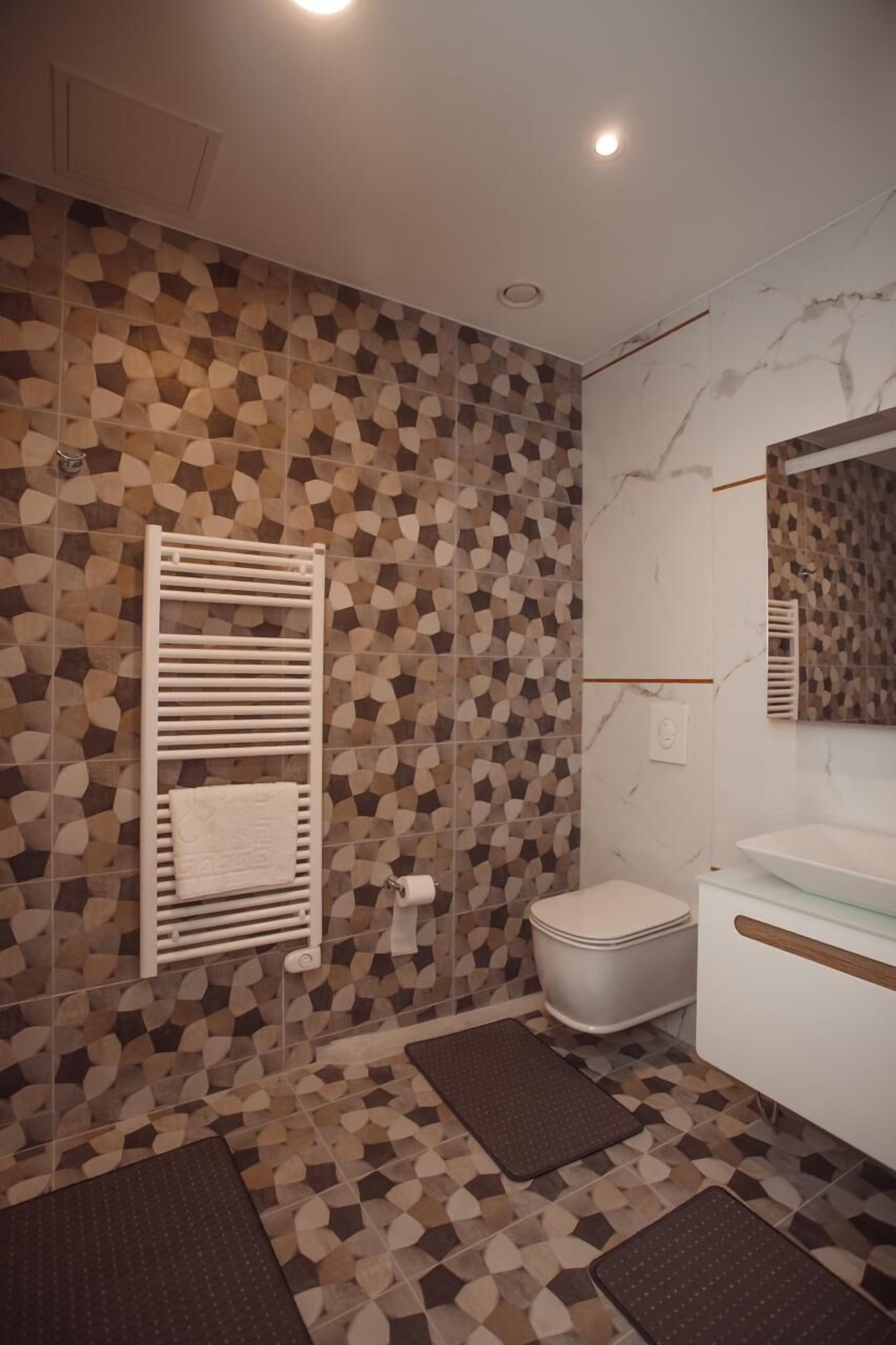 Une salle de bain avec un mur recouvert de carreaux à motifs, un porte-serviettes blanc, des toilettes et un lavabo avec un miroir.