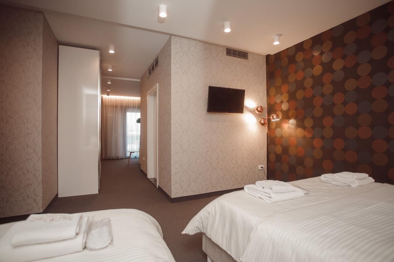 A hotel room with two beds, a television mounted on the wall, and a patterned wallpaper on the right wall.