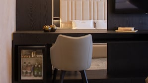 A hotel room with a dark wood panel wall, a large mirror, a bed with white bedding, a TV mounted on the wall, and a minibar with beverages. - Hotel Chicago (Shkodër)