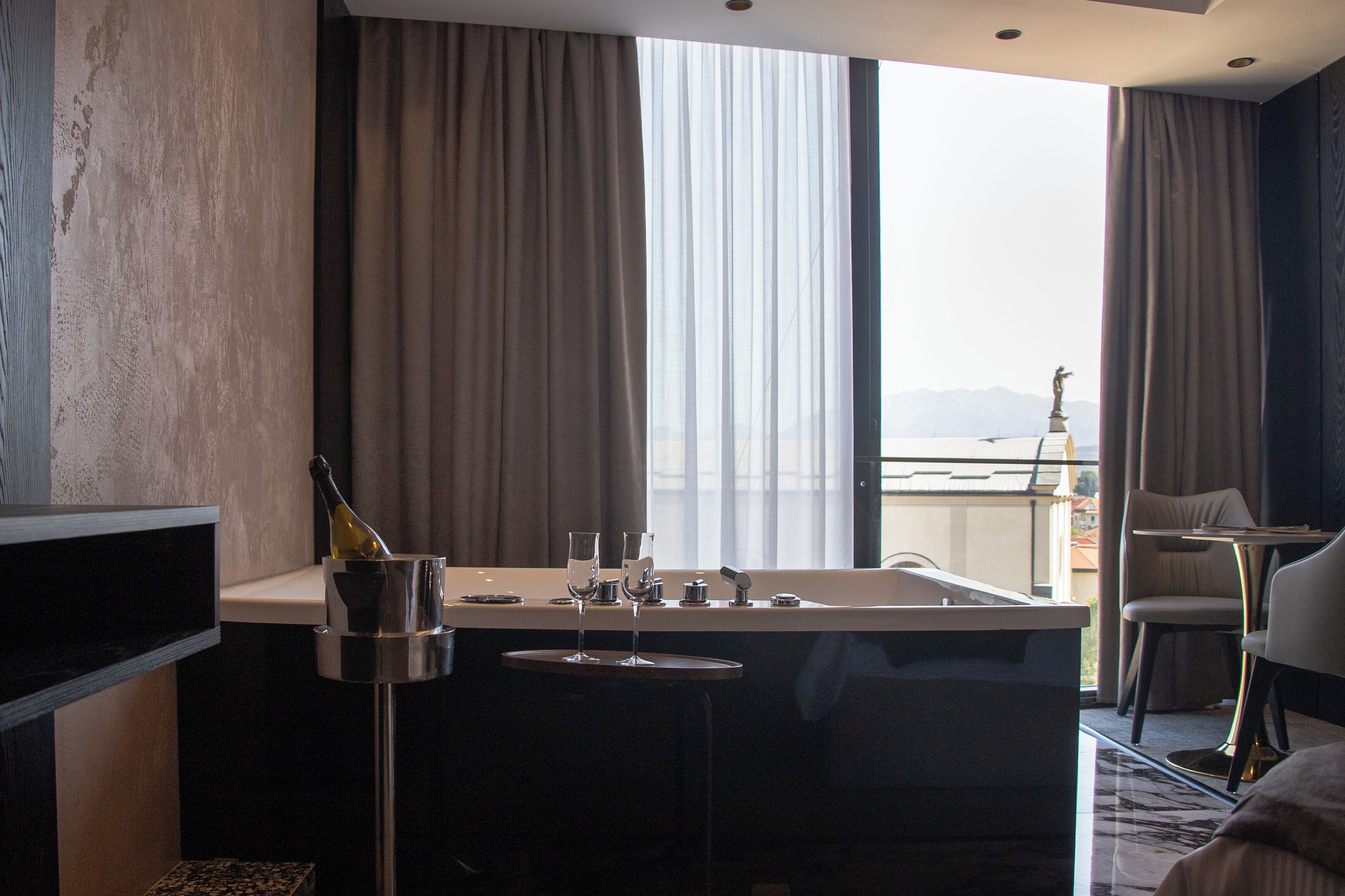 Een moderne hotelkamer met een groot raam, een badkuip, een minibar en een zithoek.