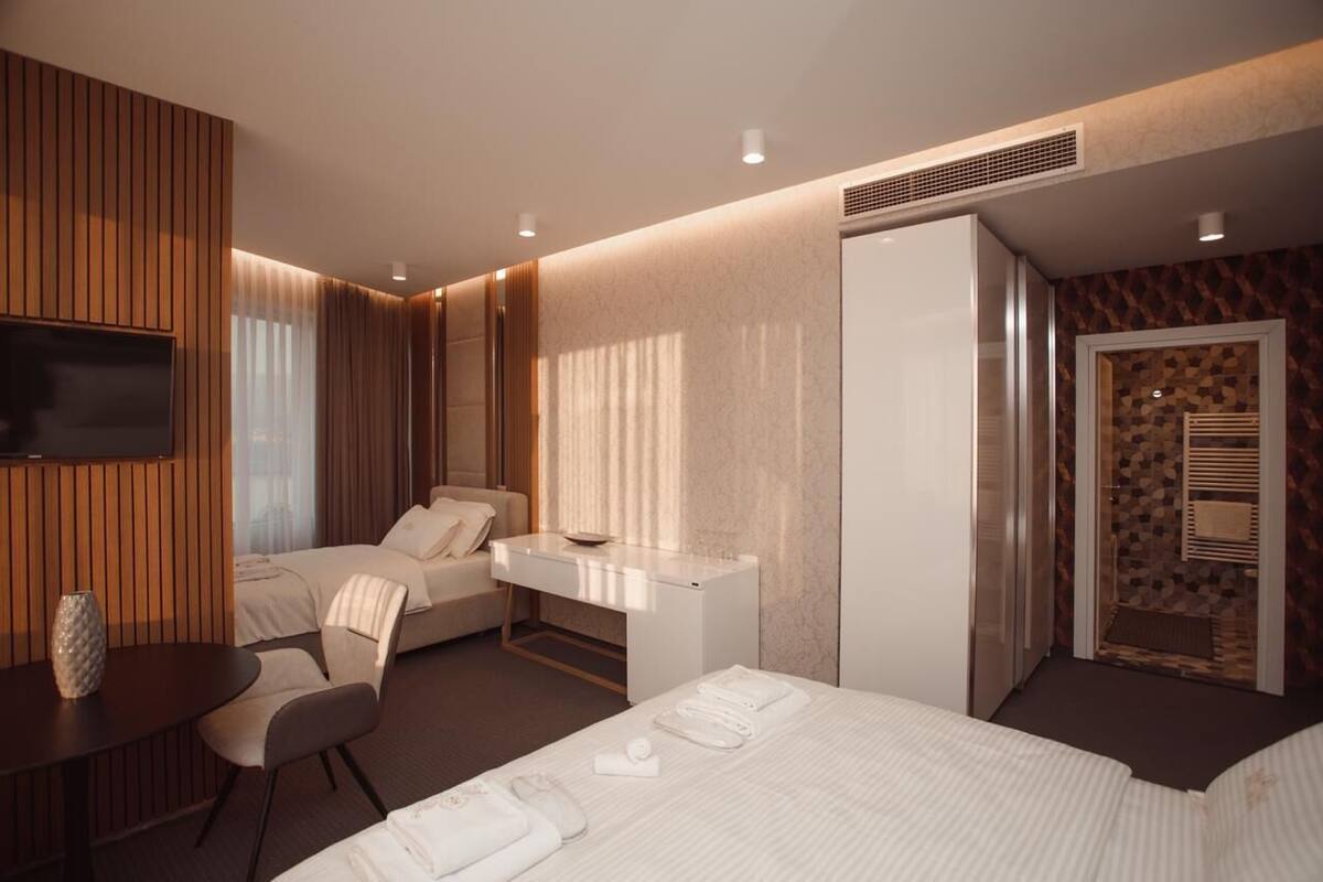 A hotel room with a bed, two bedside tables, a desk, a chair, a TV, and a shower area.