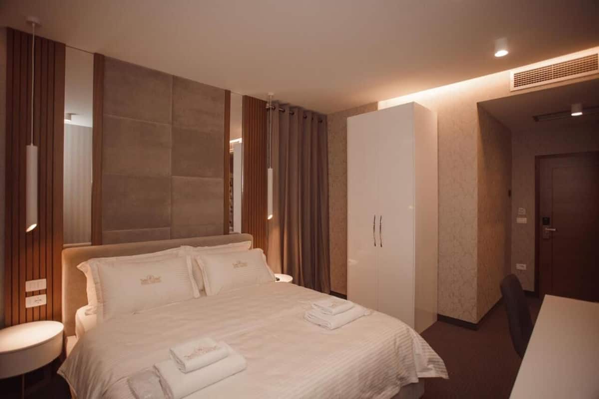 A hotel room with a large bed, a wardrobe, a desk, and a chair.