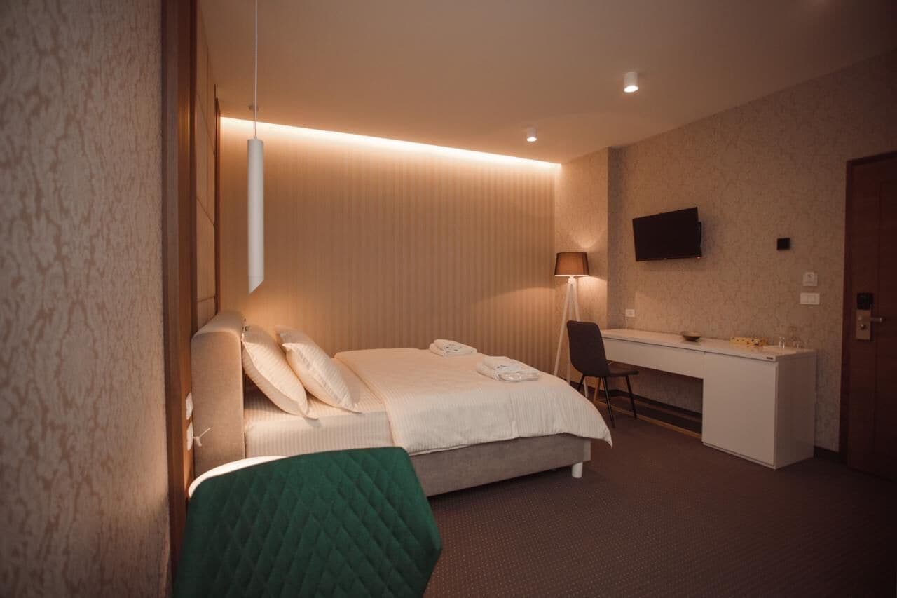 Quarto de hotel com cama, secretária, cadeira e televisão na parede.