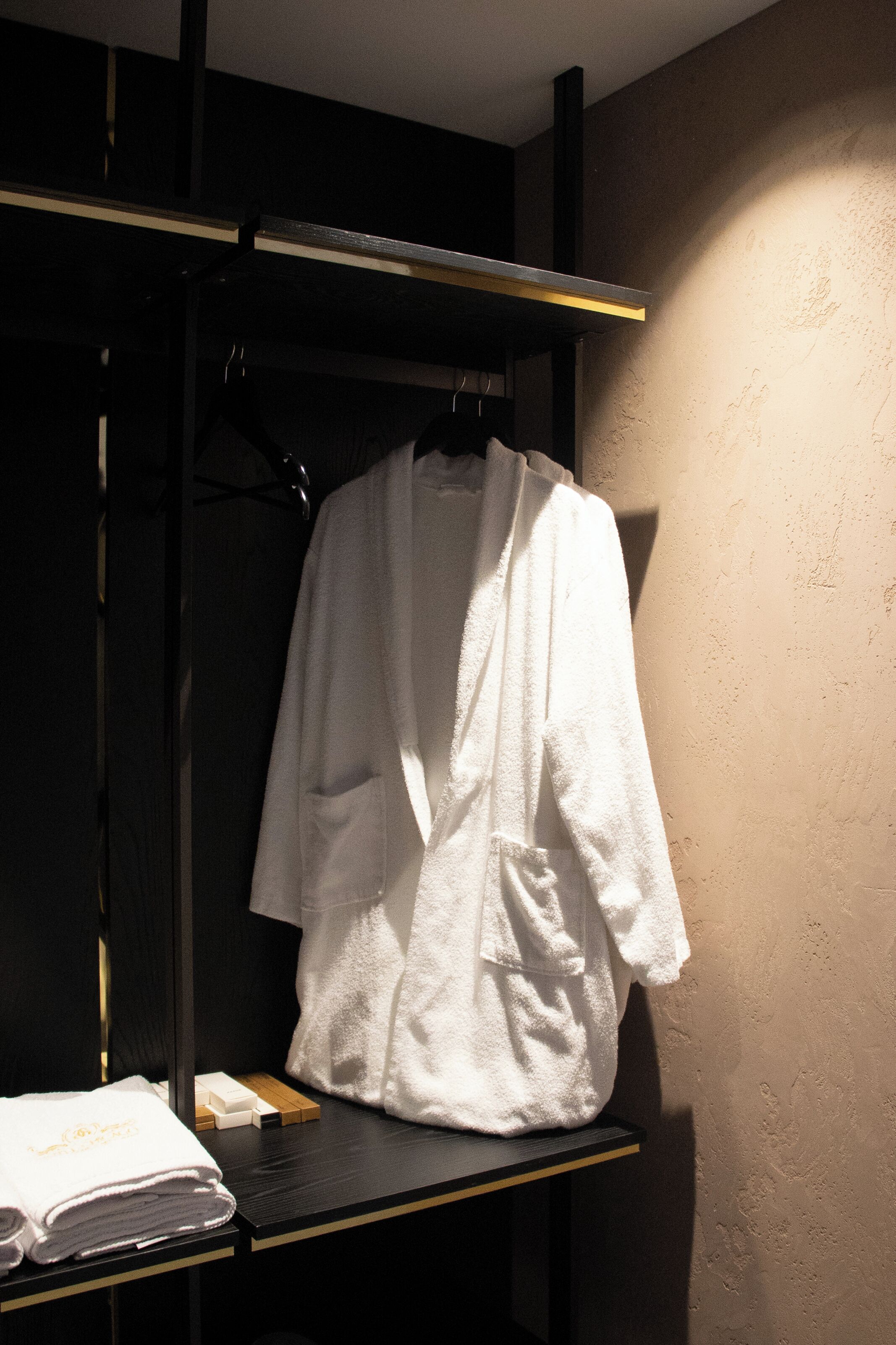 A white robe hanging on a rack in a dimly lit room with a textured wall.