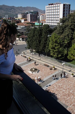 A hotel with a prominent sign, a paved courtyard with benches, and a street view with vehicles.