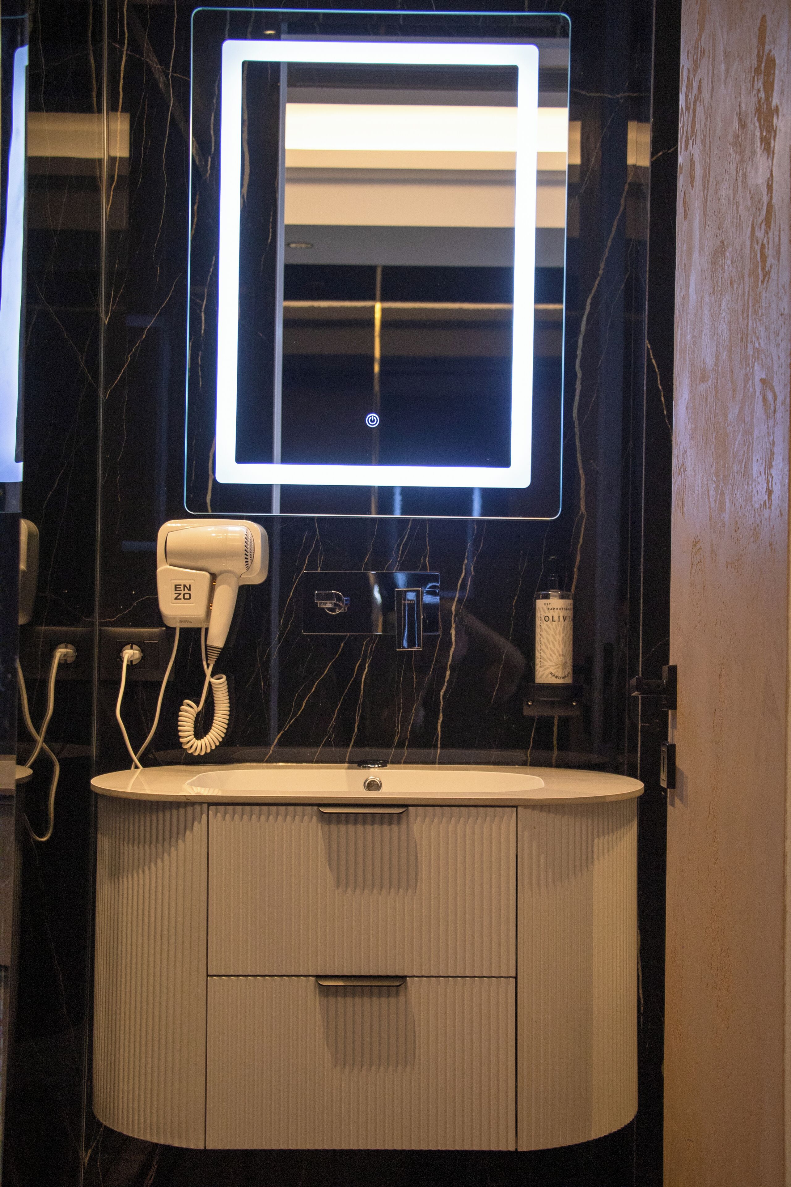 Une salle de bain équipée d’un meuble-lavabo, d’un sèche-cheveux, d’un miroir et d’une bouteille d’huile d’olive.