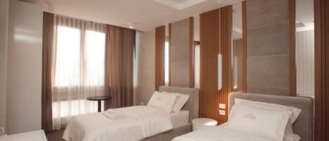 Una habitación de hotel con dos camas, una mesita redonda y un ventanal grande con cortinas.