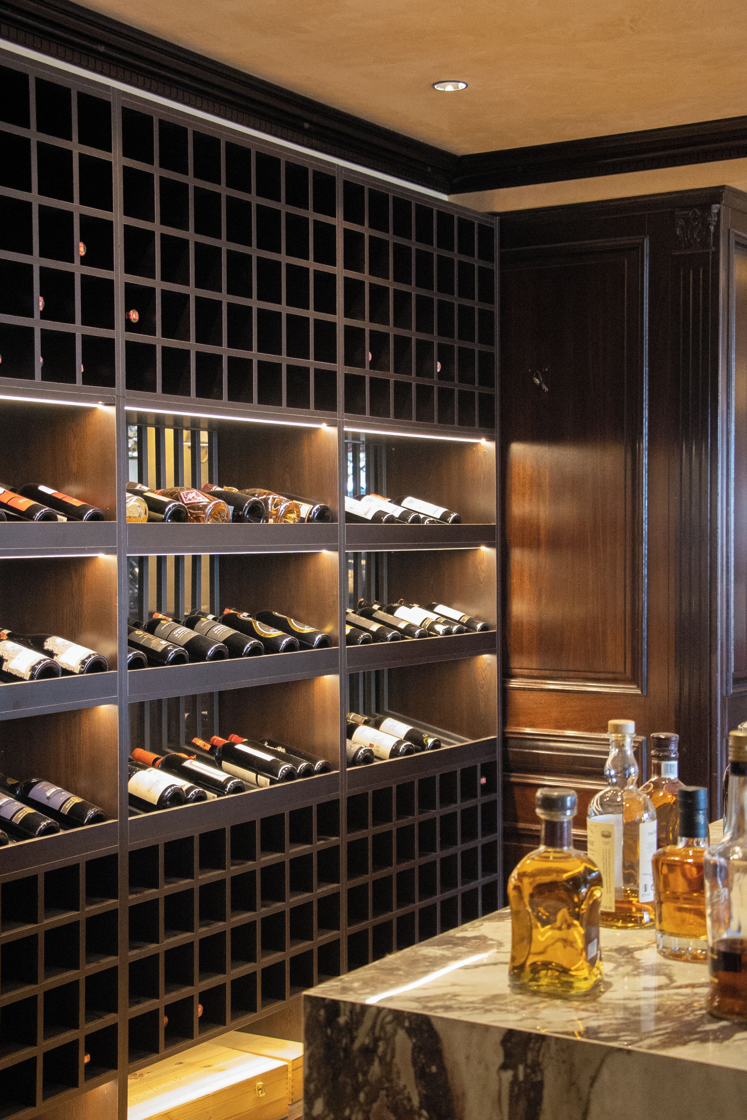 A wine cellar with shelves of wine bottles and a marble countertop with additional bottles.