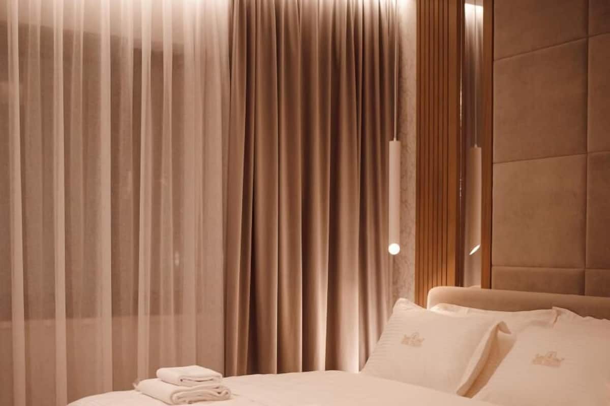 A hotel room with a bed, a chair, a desk, and a large window with curtains.