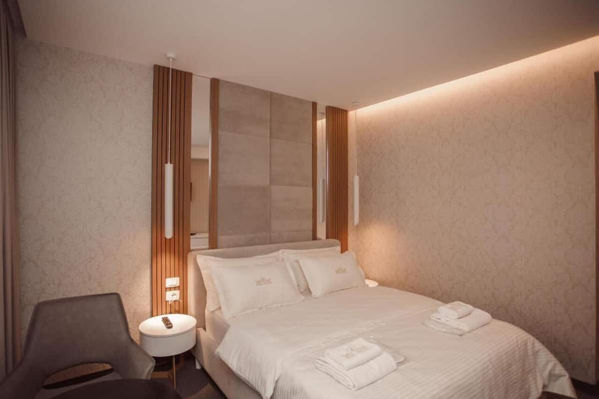A hotel room with a bed, a chair, a bedside table, and a lamp.