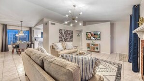 A spacious living room with a large sofa set, a dining area with a table and chairs, a kitchen in the background, and a TV mounted on the wall. - YOUR private Desert Getaway with FREE Heated Pool! (Phoenix)