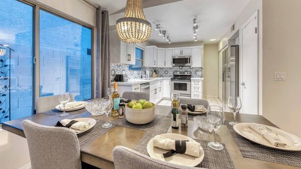A modern kitchen with white cabinets, a large island, and a dining area with a table set for four. - YOUR private Desert Getaway with FREE Heated Pool! (Phoenix)