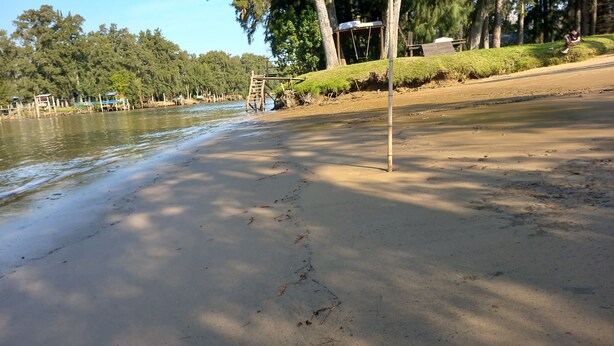 A sandy beach with a wooden structure and a metal pole. - Cabaña del humedal (Partido de Tigre)