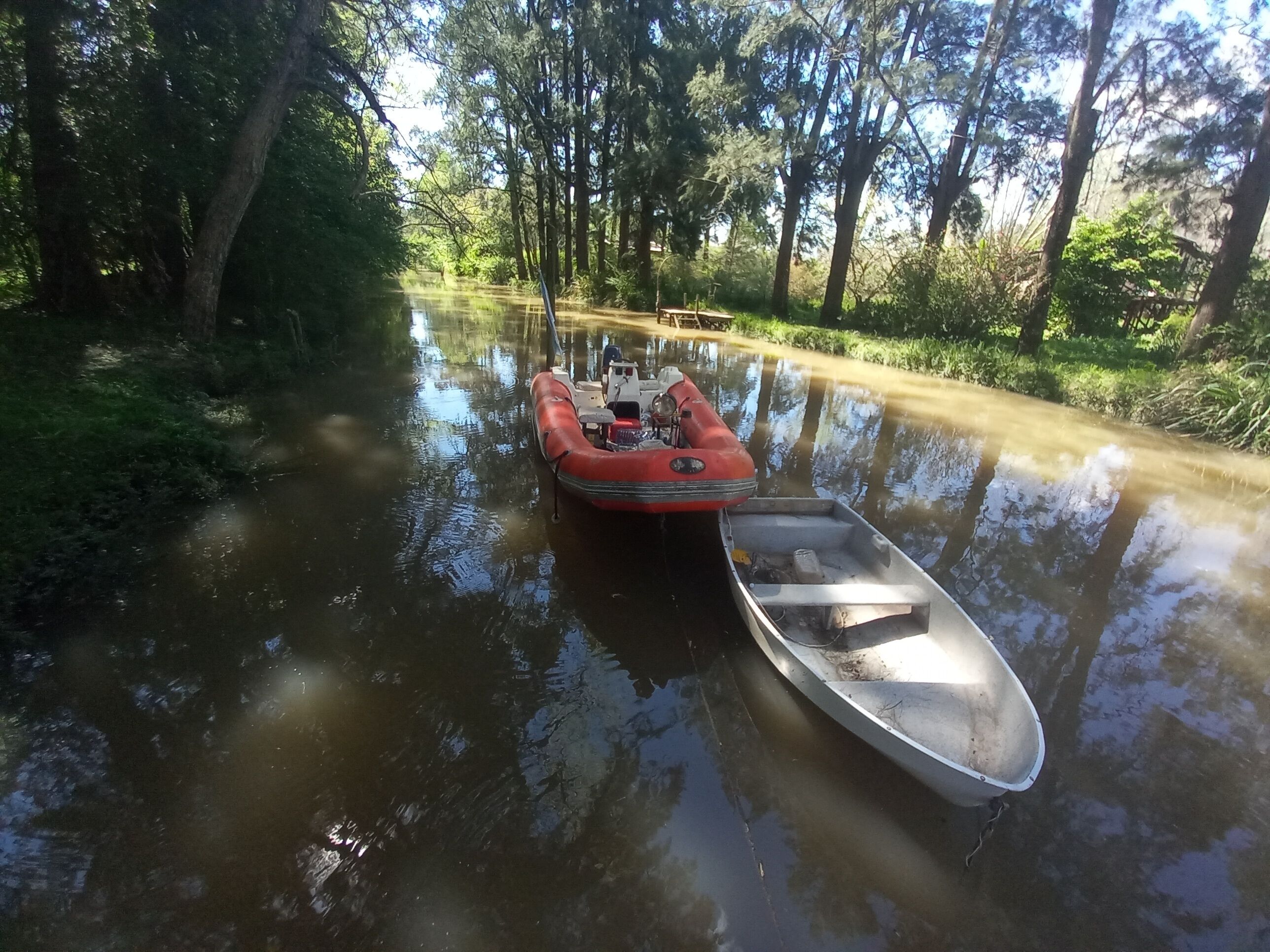 A narrow waterway with a red inflatable boat and a metal canoe docked on the right.
