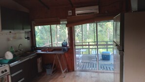 A cabin kitchen with a wooden interior, a large window, and a view of a deck and trees. - Cabaña del humedal (Partido de Tigre)