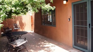 An outdoor patio with a table and chairs, a door with a window, and a wall-mounted light.