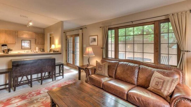 A cozy living room with a leather sofa, a wooden coffee table, and a kitchen area with a bar counter.