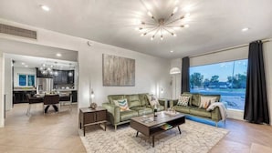 A spacious living room with a green sofa, a coffee table, and a large window offering a view of the outdoors. - Mid-Century Modern Charmer with FREE heated pool! (Phoenix)