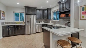 A modern kitchen with dark cabinetry, stainless steel appliances, and pendant lighting. - Mid-Century Modern Charmer with FREE heated pool! (Phoenix)
