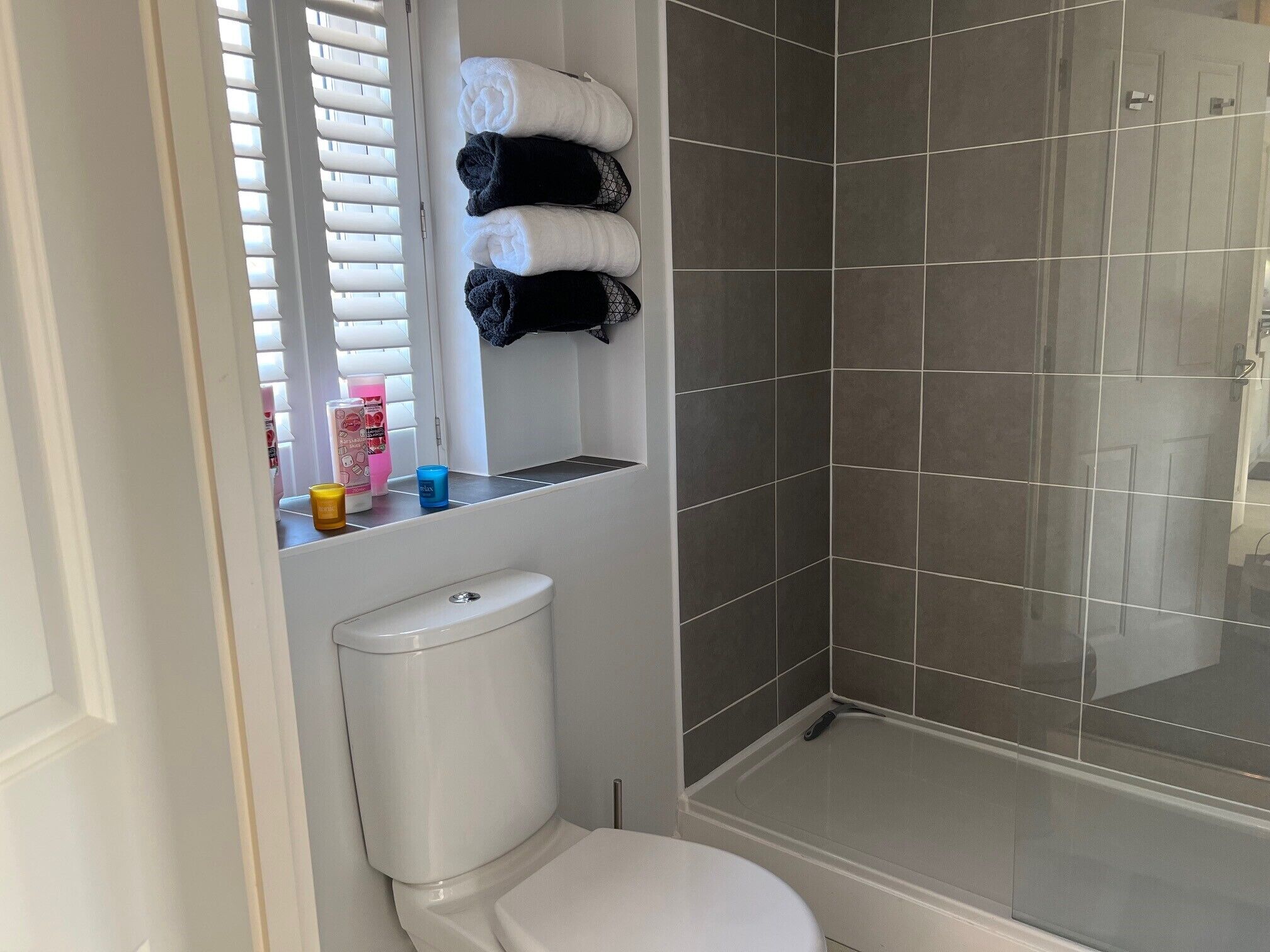 Une salle de bain comprenant des toilettes, une douche avec une porte en verre et une étagère avec des serviettes et des articles de toilette.