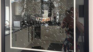 Une œuvre d’art encadrée représentant une figure portant un casque avec une surface réfléchissante, qui pourrait être un miroir, dans une pièce où se trouvent un four à micro-ondes et des placards.