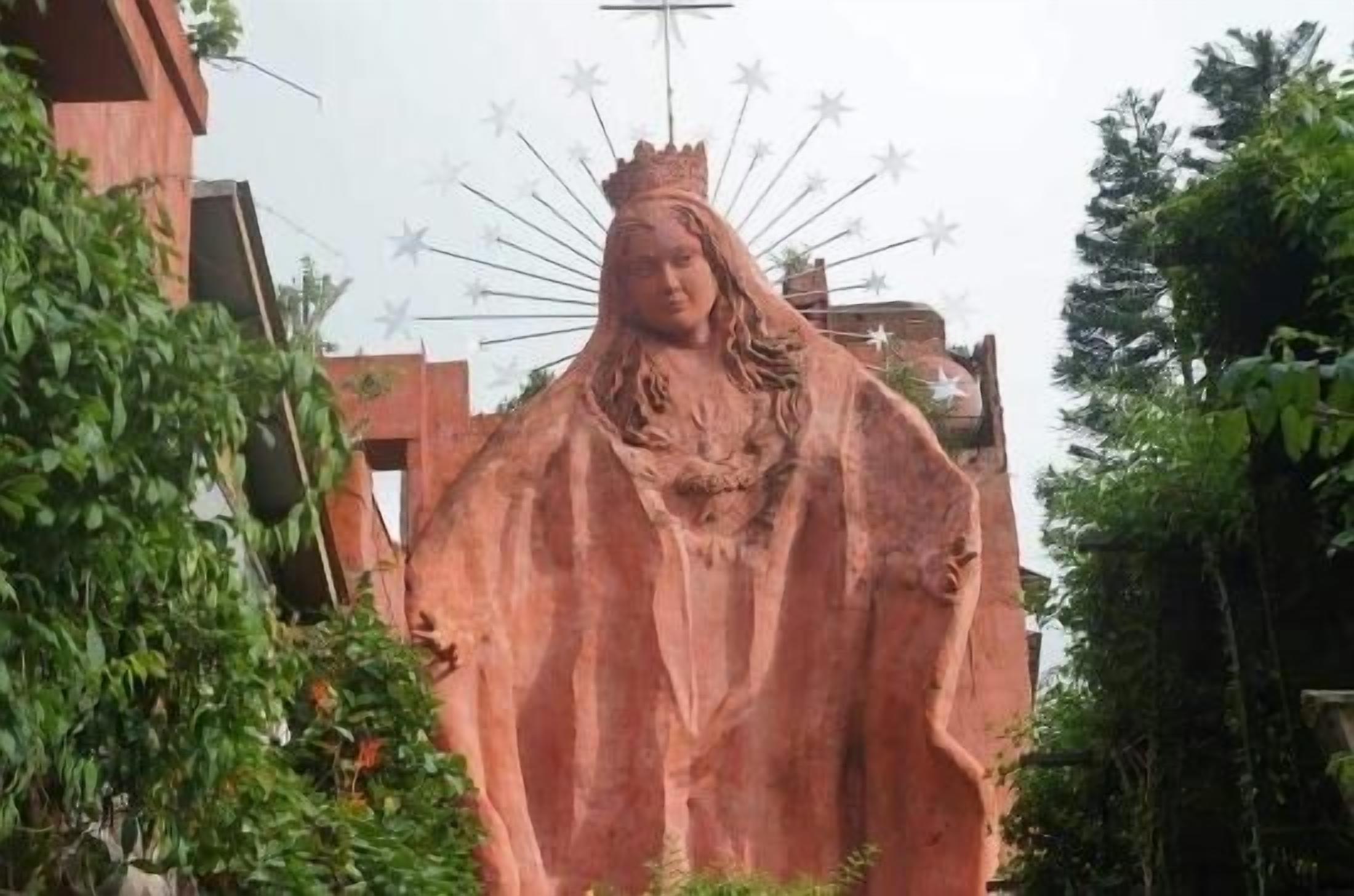 A large outdoor statue of a figure with a crown, surrounded by greenery and buildings.