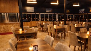 A restaurant with wooden tables and chairs, a number 6 sign on a table, and a view of the city at night through large windows. - Whitestone Hotel (Ürgüp)
