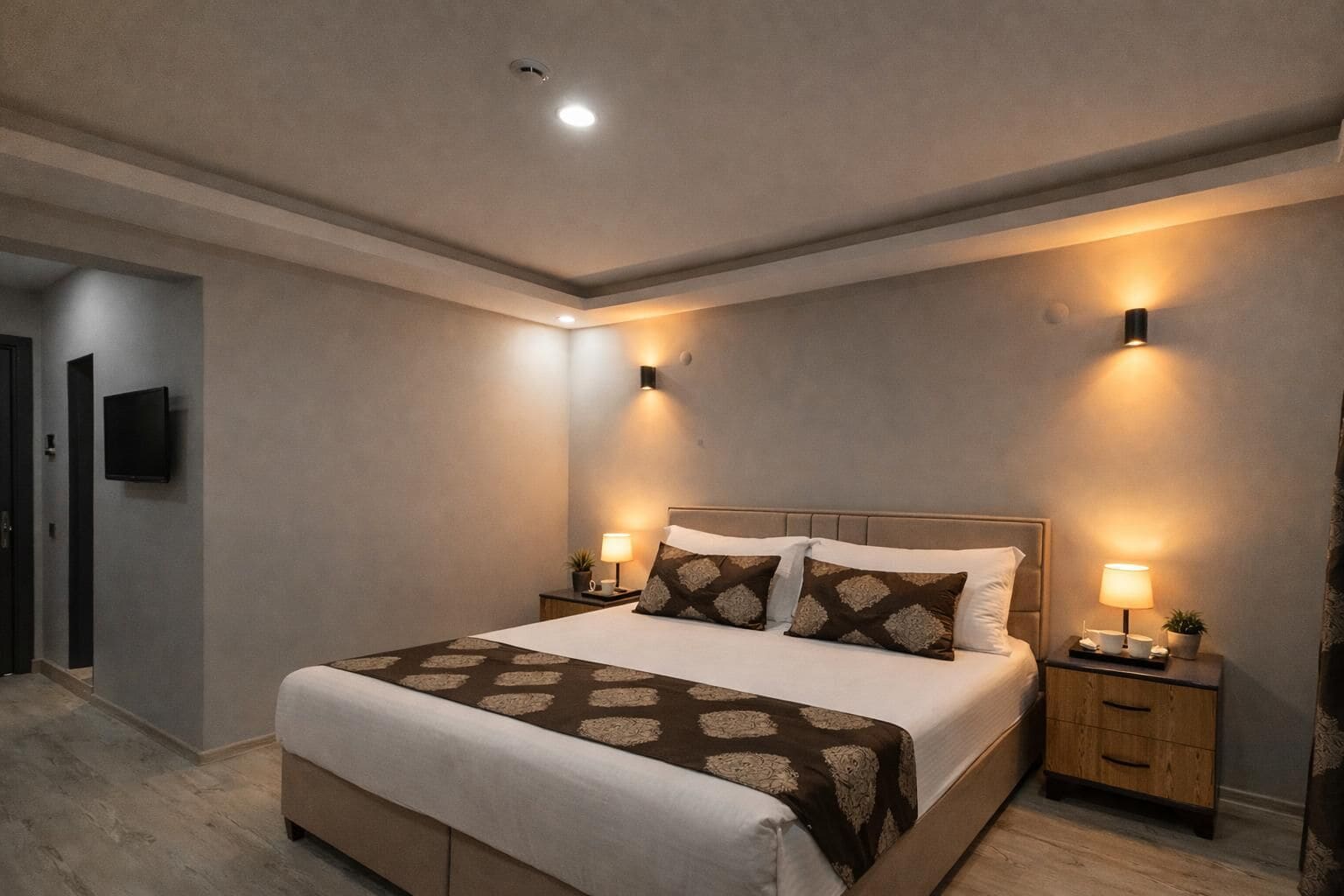 A modern bedroom with a large bed, two bedside tables with lamps, a flat-screen TV on the wall, and a neutral color scheme.