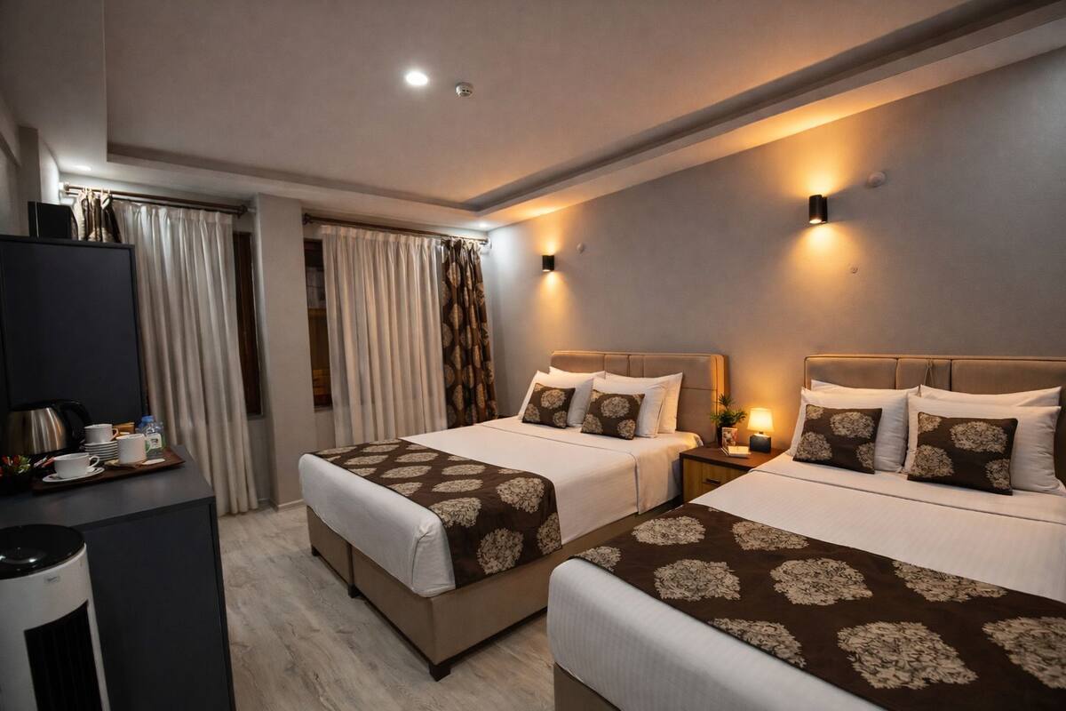 A hotel room with two beds, a desk with a kettle, and a wardrobe.