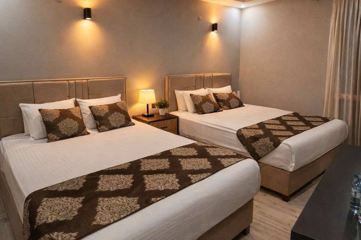 A hotel room with two beds, each with a headboard, bedside tables, and lamps.