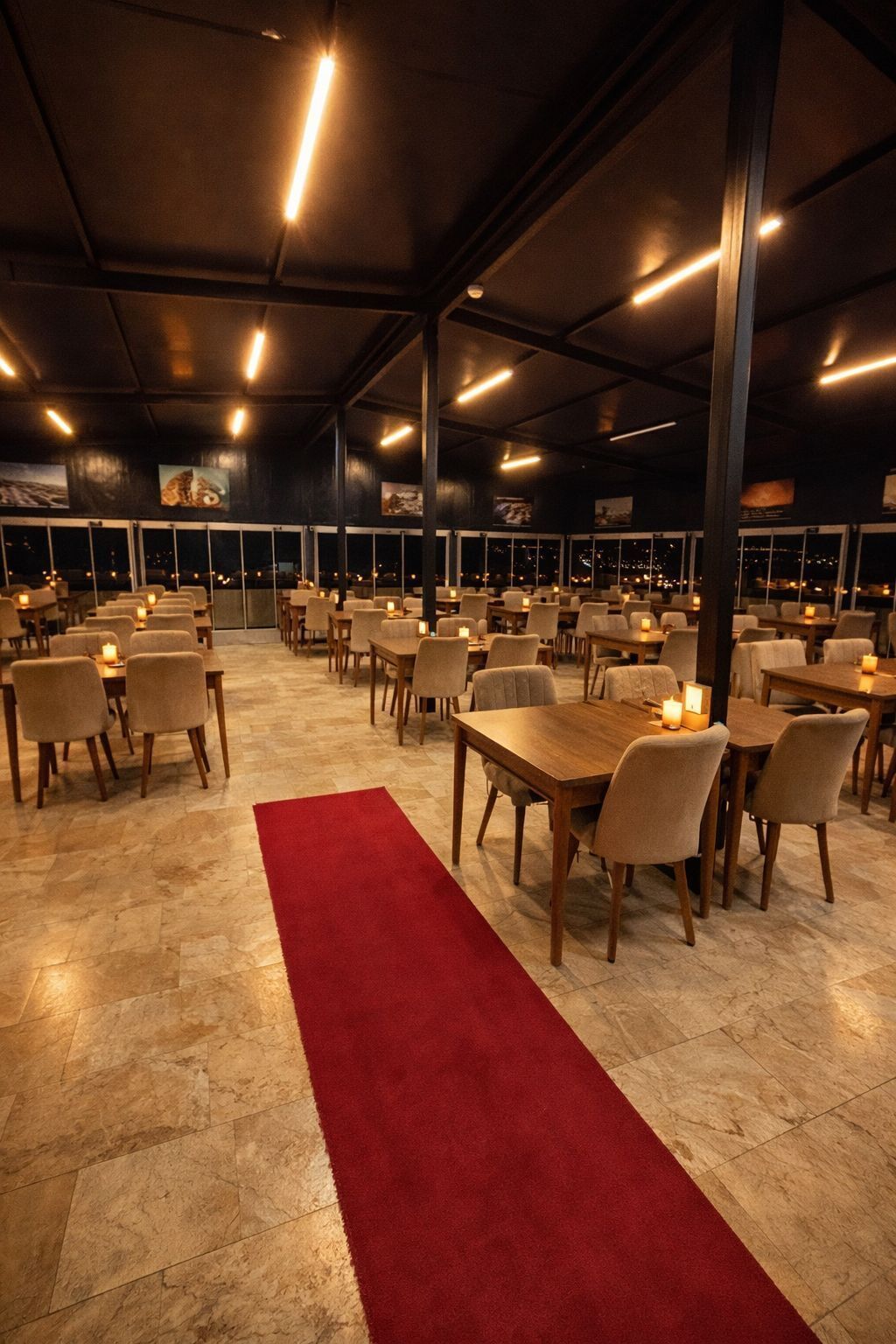 A spacious indoor dining area with multiple tables and chairs, a red carpet, and large windows with city views.