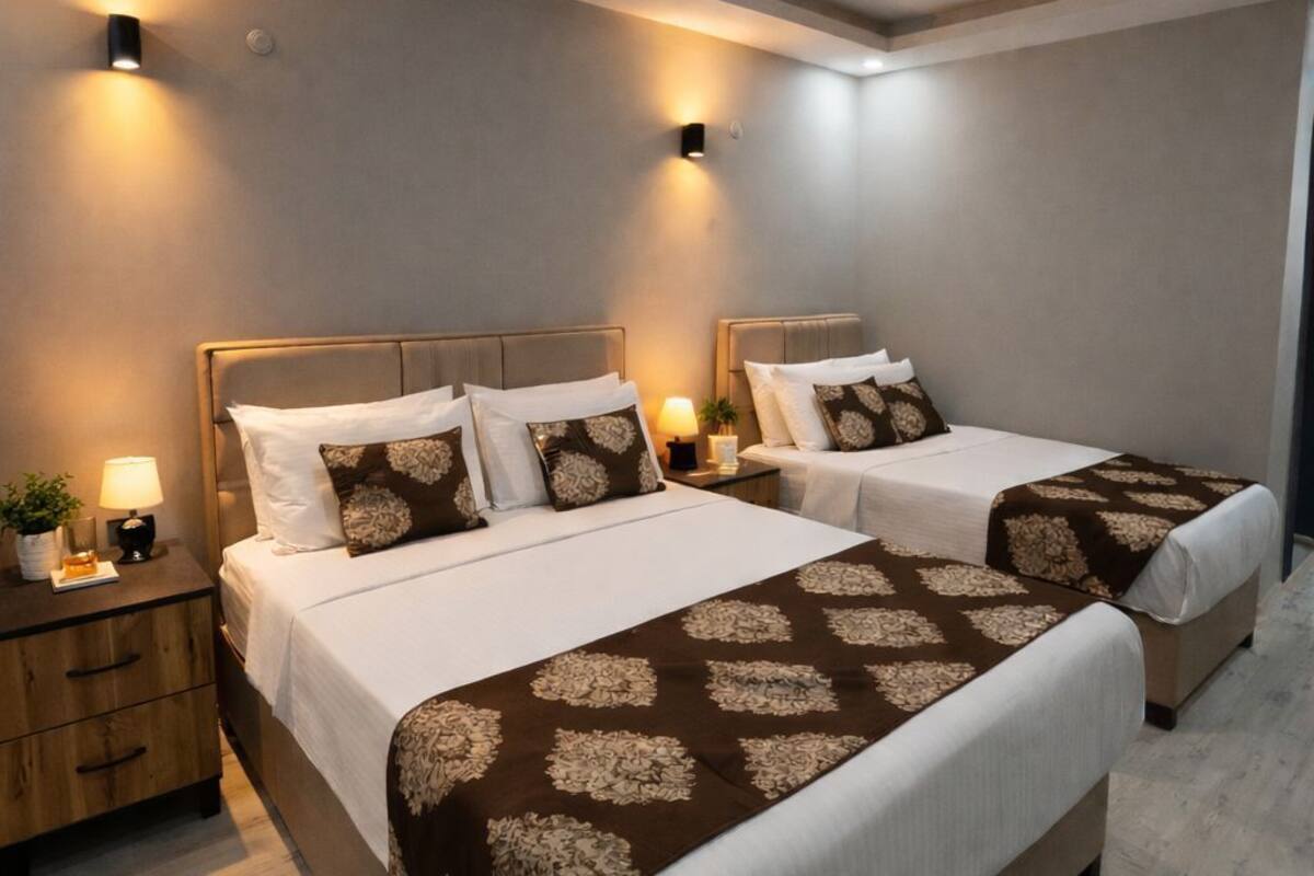 A hotel room with two beds, a nightstand, and wall-mounted lights.