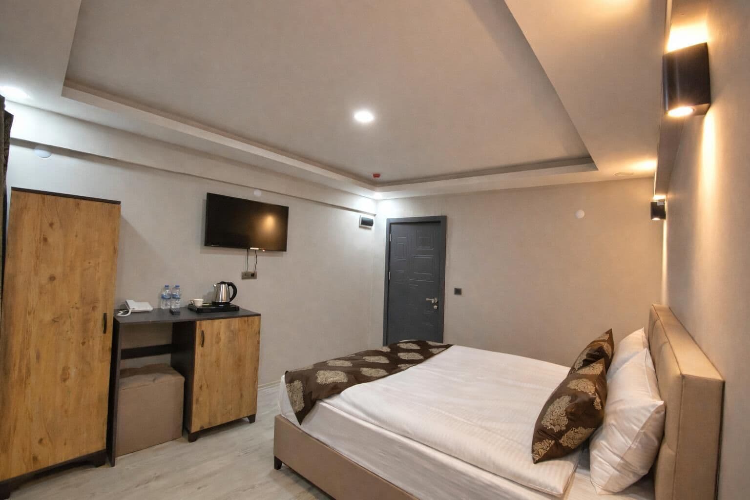 Een slaapkamer met een bed, een houten kledingkast, een bureau met een flatscreen televisie en een deur.
