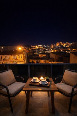 Une terrasse avec deux chaises et une table, deux tasses de café et une bougie allumée.