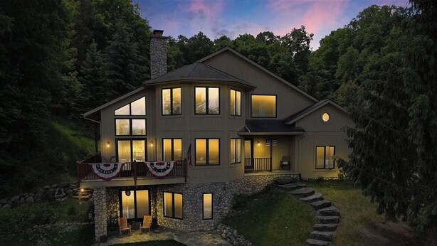 A modern two-story house with a stone foundation, multiple windows, and a well-lit front porch.