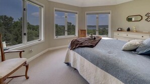 A bedroom with a large bed, two windows, a chair, and a dresser.