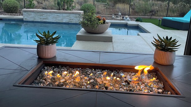 A pool area with a fire feature, potted plants, and a view of the surrounding landscape.